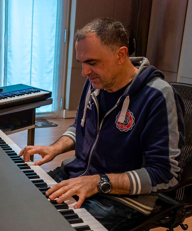 Raniero Gaspari al lavoro nel suo studio di registrazione, seduto alla tastiera e di fronte a più schermi e strumenti, concentrato sull'editing musicale.